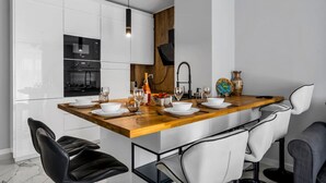 A modern kitchen with white cabinets, a wooden island, and a dining area with white chairs. - Białołęka Apt - 61m2, Parking & Balcony - by Rentujemy (Warszawa)