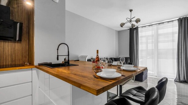 A modern kitchen with a wooden countertop, black faucet, and a dining area with a table set for four. - Białołęka Apt - 61m2, Parking & Balcony - by Rentujemy (Warszawa)