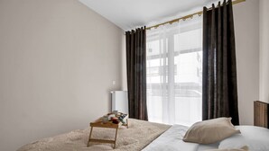 A modern bedroom with a large bed, a bedside table with a tray, and a window with dark curtains. - Białołęka Apt - 61m2, Parking & Balcony - by Rentujemy (Warszawa)