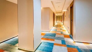 Ein Hotelgang mit farbigem Teppich und Türen an beiden Seiten, der sich weit in die Länge zieht.