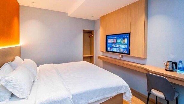 Ein Hotelzimmer mit Bett, Wand-Fernseher, Schreibtisch mit Stuhl und einer kleinen Ablage mit Gegenständen.