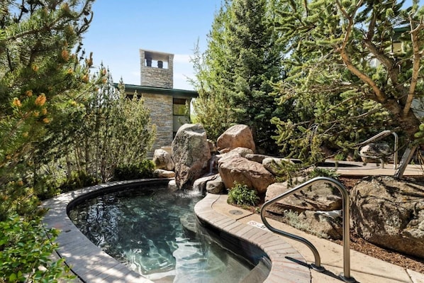 Relax in a serene hot tub surrounded by lush trees and a historic stone structure.