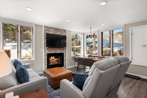 Cozy living room with a fireplace, flat-screen TV, and dining area offering a view of the surrounding landscape.