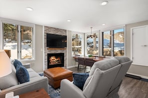 Cozy living room with a fireplace, flat-screen TV, and dining area offering a view of the surrounding landscape.