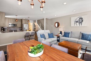 Relax in this stylish living space with a dining table, sofa, and ottoman, plus a staircase leading to an upper level.