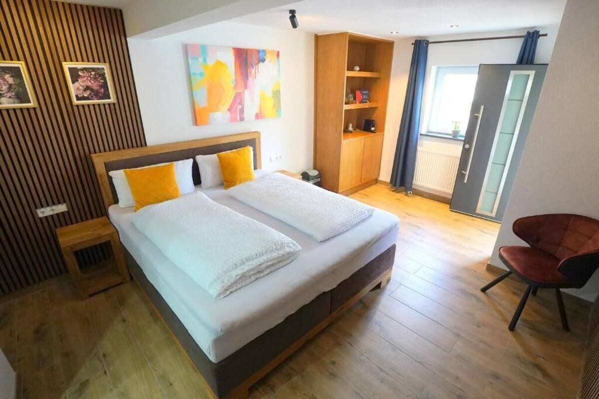 Une chambre à coucher avec un grand lit, un plancher en bois, une armoire, une chaise et une fenêtre avec des rideaux.