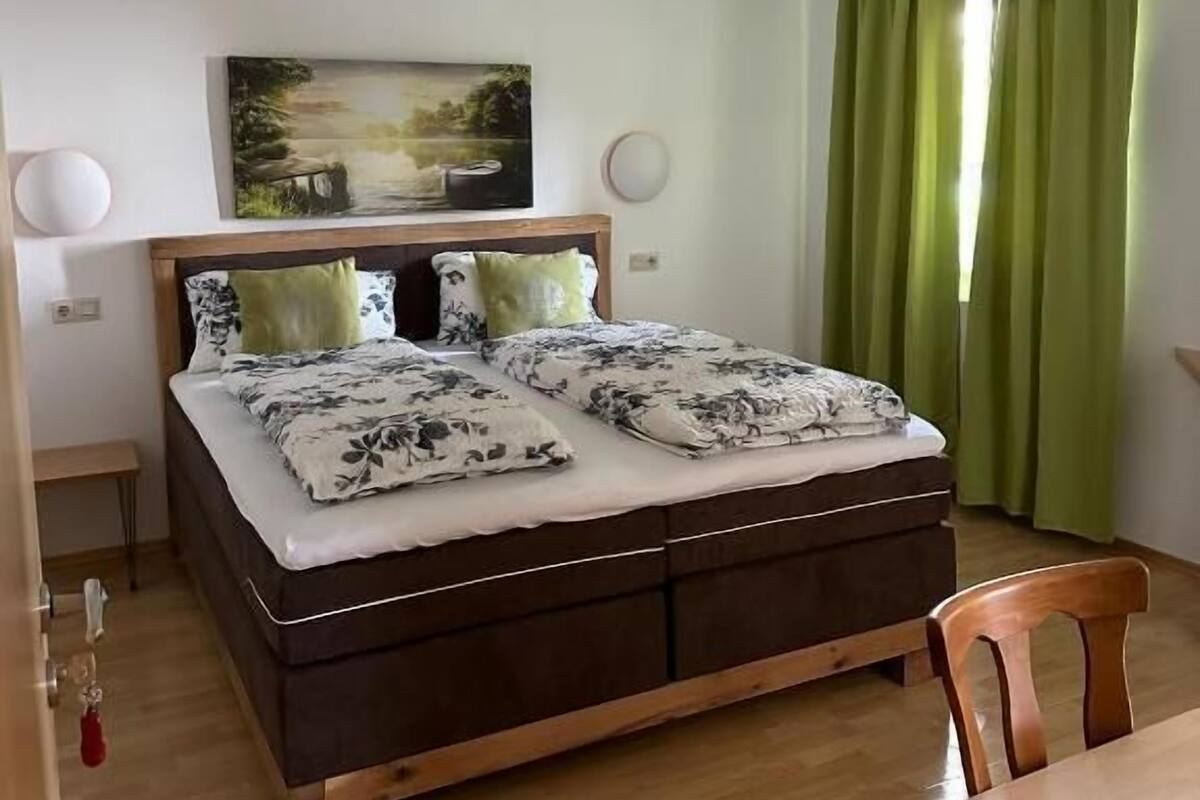 Une chambre à coucher avec un lit, un tableau au mur, un rideau vert et un plancher en bois.