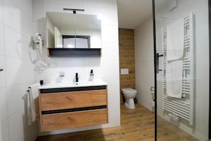 Un baño moderno con un tocador blanco, un espejo, un inodoro y una zona de ducha.