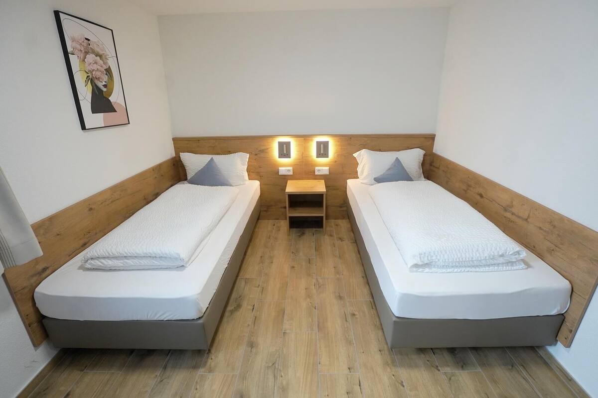 Une chambre double avec deux lits simples, des têtes de lit en bois, des tables de chevet et des lampes fixées au mur.
