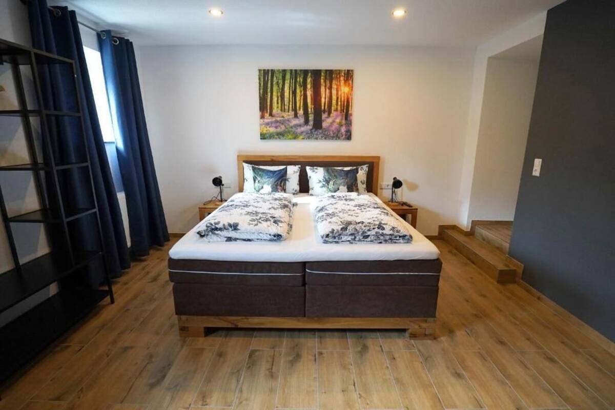 Une chambre à coucher avec un lit en bois, deux tables de chevet, un tableau représentant une forêt et un plancher en bois.