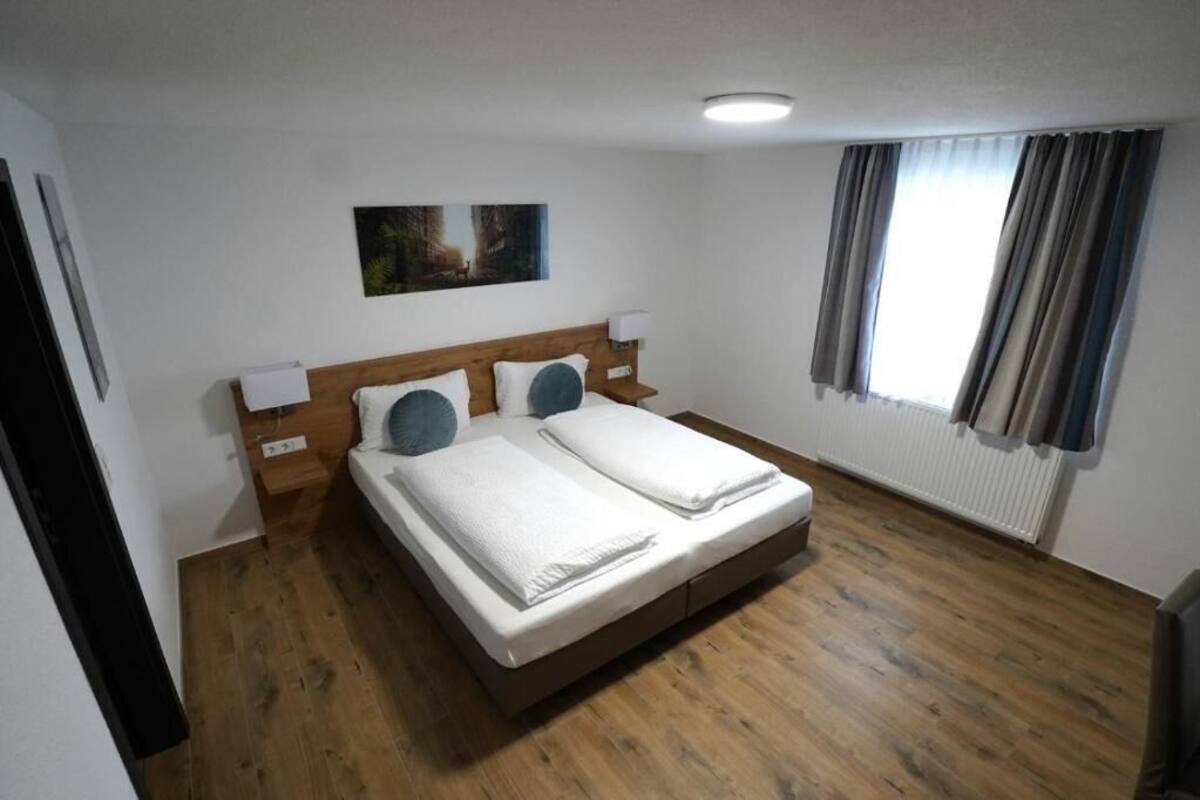 Un lit double avec deux oreillers, une tête de lit en bois, des lampes de chevet et un tableau au mur.