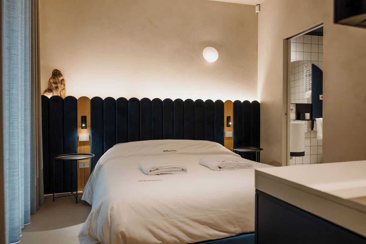 Une chambre d’hôtel avec un lit, une table de chevet, une lampe et une salle de bain visible à travers une porte ouverte.