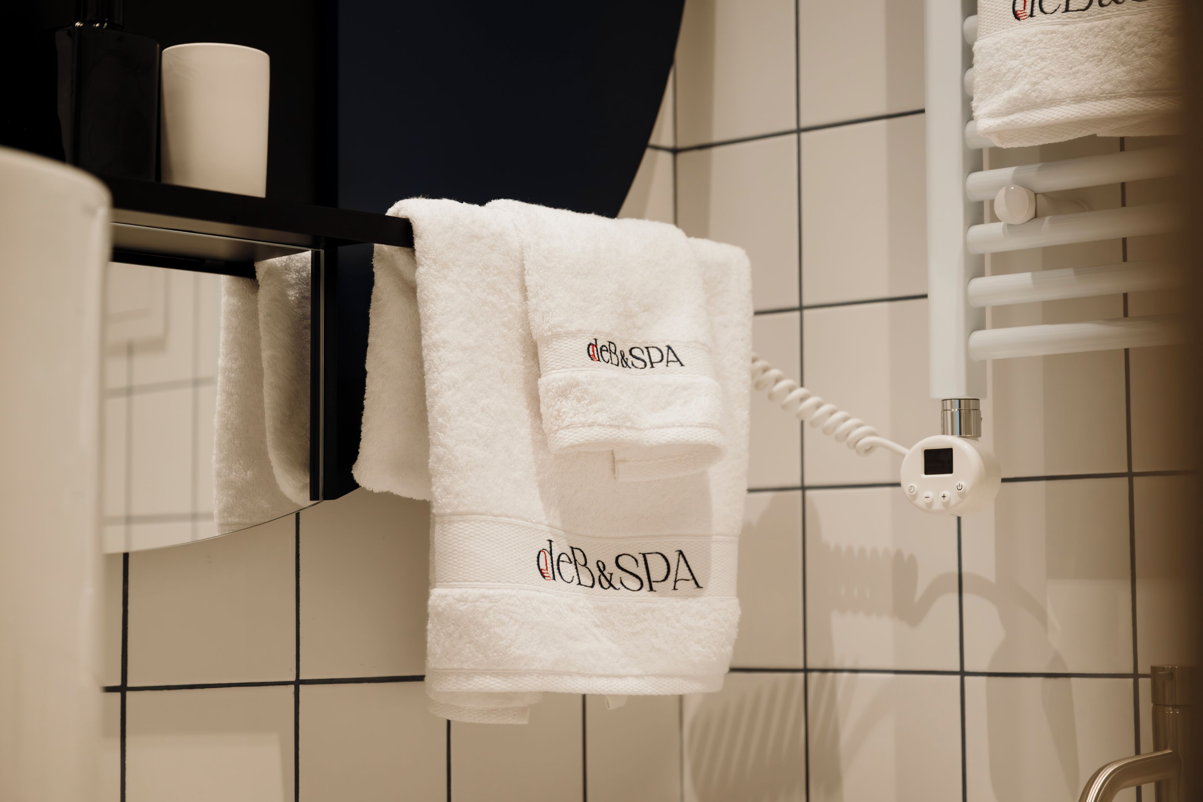 A bathroom with a towel rack holding two white towels with "CB&SPA" embroidered on them.