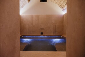 A spa room with a large bathtub, a small window, and a stone wall.