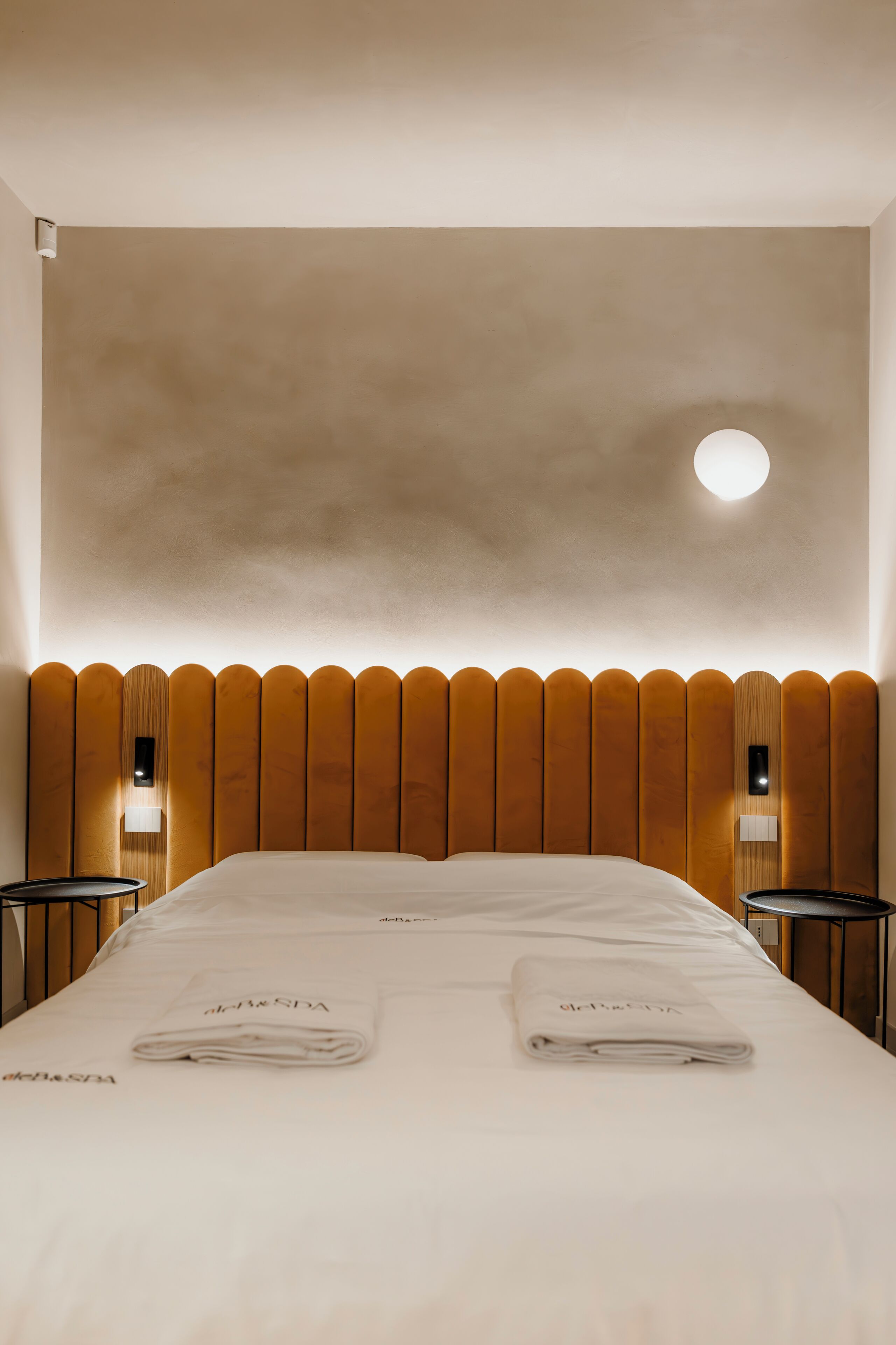 Habitación de hotel con una cama grande, dos mesitas de noche y una lámpara fijada a la pared.