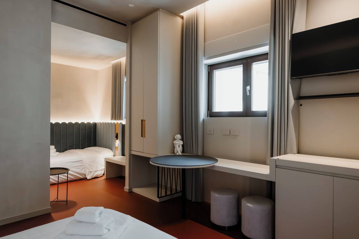 Une chambre d’hôtel moderne, équipée d’un lit, d’une table de chevet et d’une petite table ronde dont le plateau est bleu.