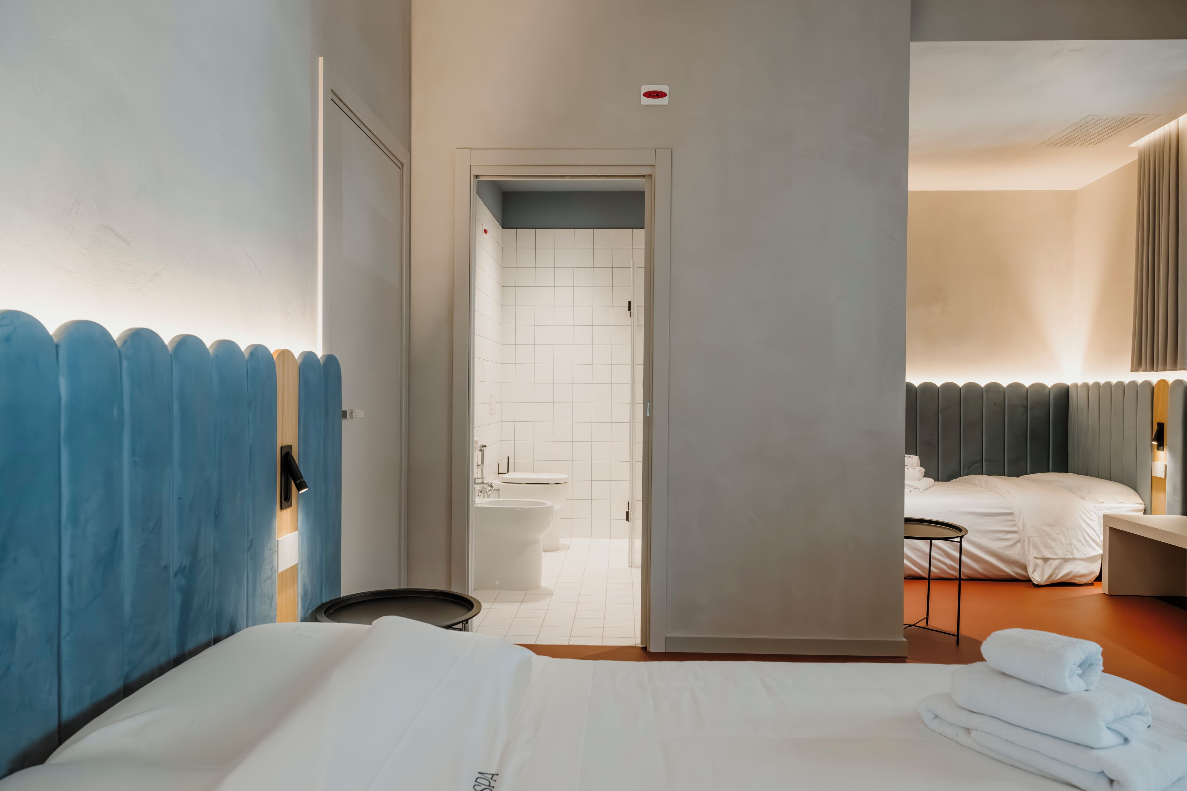A hotel room with a bed, a small table, a bathroom with a toilet and sink, and a shower area.