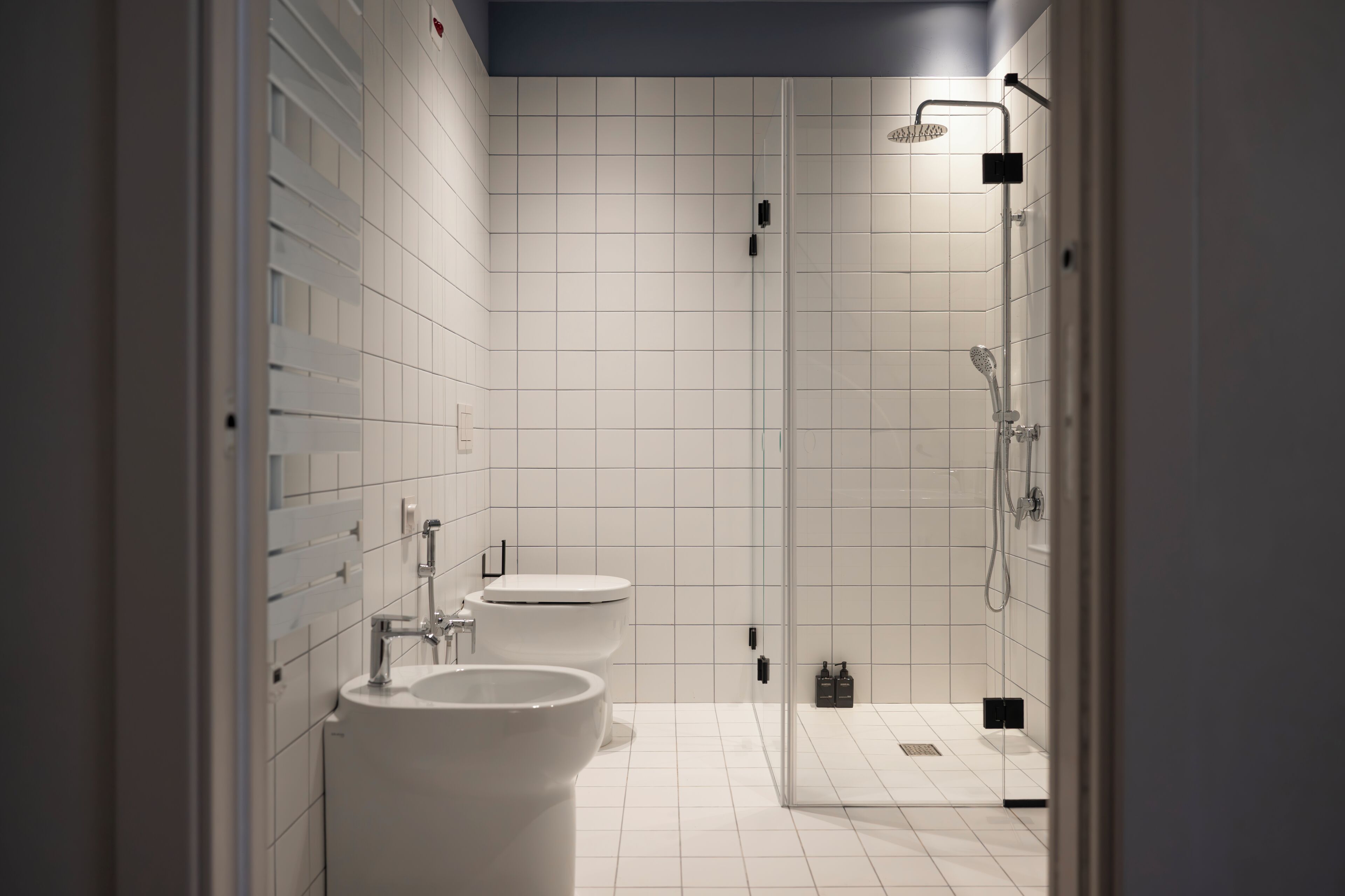 Une salle de bain moderne avec des carreaux blancs, une douche en verre et deux lavabos.
