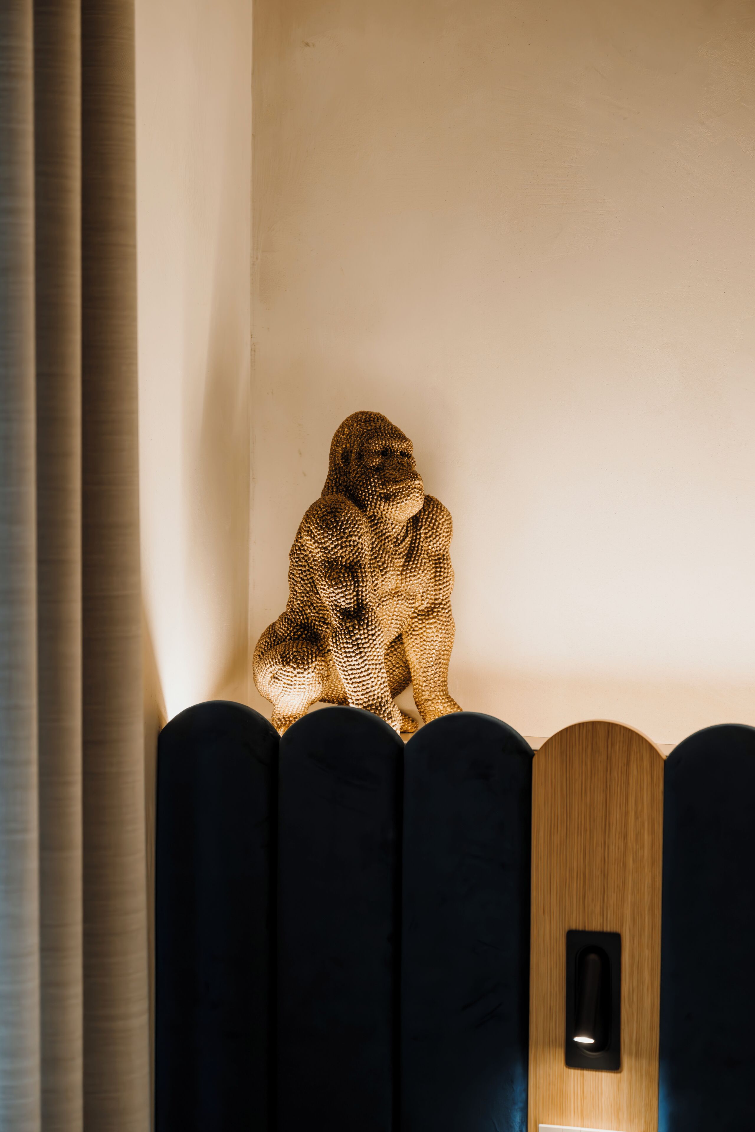 A room with a unique textured wall sculpture, a wooden panel with a light switch, and a dark-colored seating area.