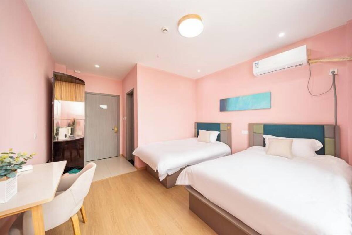A hotel room with two beds, a desk, a chair, a wardrobe, and an air conditioning unit.