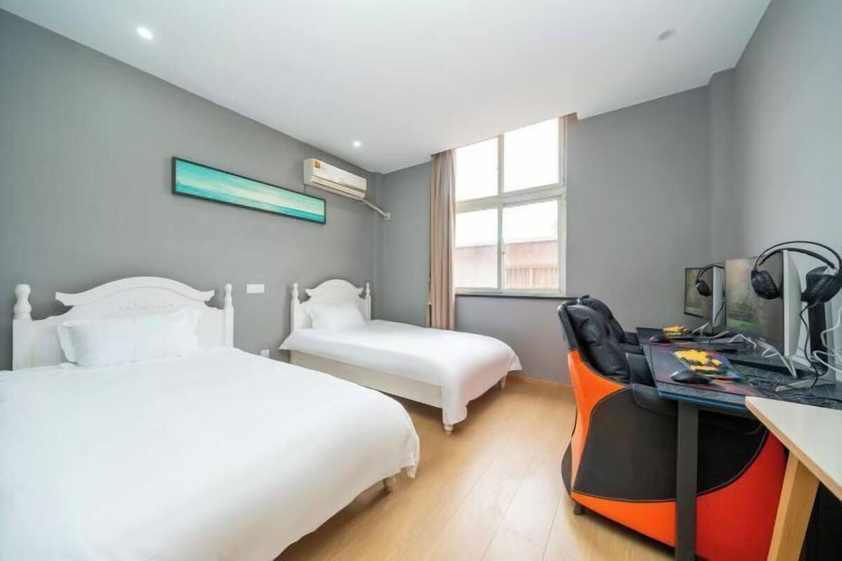 A bedroom with two beds, a desk with a computer, and a window.