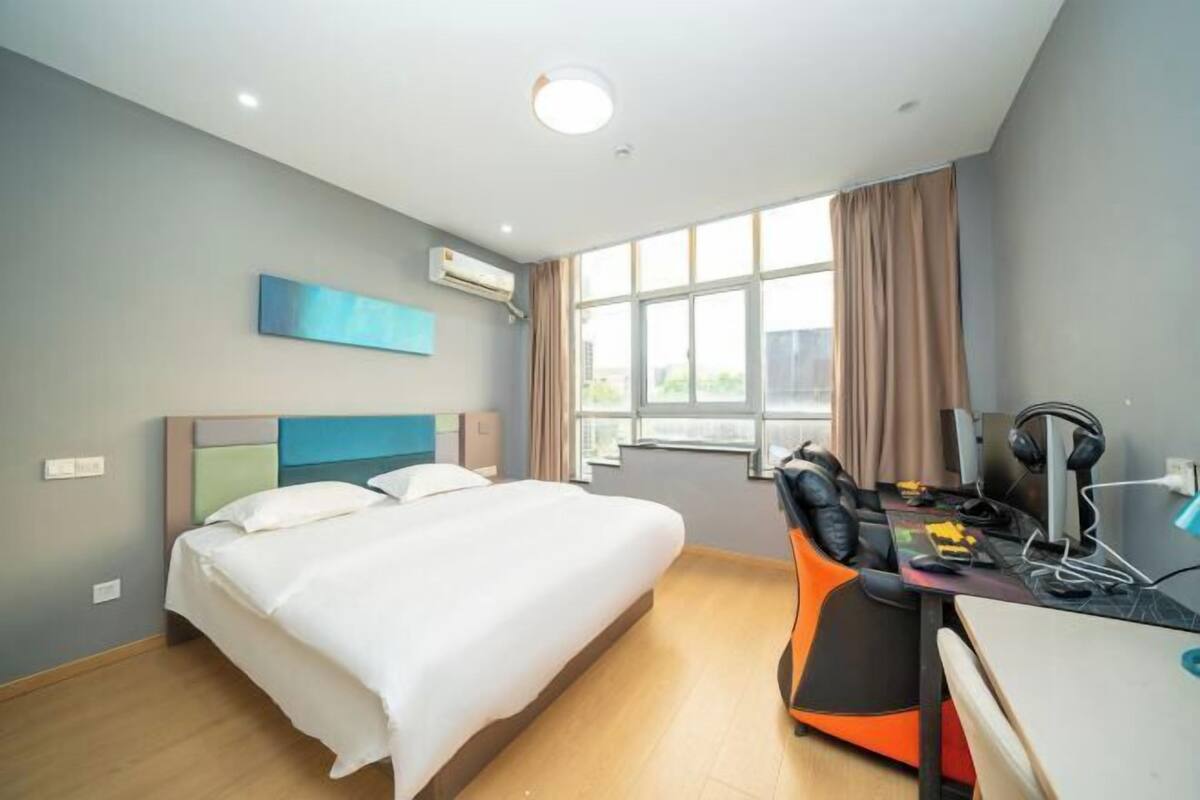 A hotel room with a bed, a desk with a computer, headphones, and a chair.