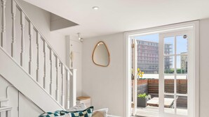 A staircase with white balusters, a wooden bench, a small table, and a large window with a view of buildings and a balcony.