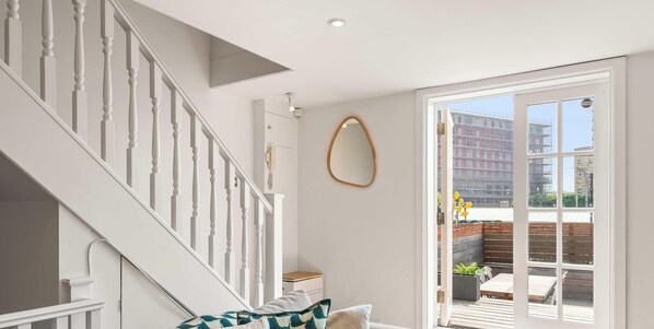 Una escalera con balaustres blancos, una puerta blanca que da a un balcón y un espejo redondo en la pared.