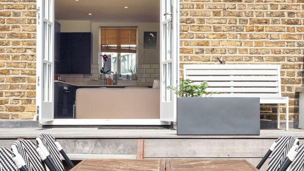 An open doorway leading to a room with a bench, a potted plant, and a view of a brick wall.