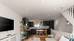 A modern living room with a flat-screen TV, a bookshelf, and a dining area with a table and chairs.