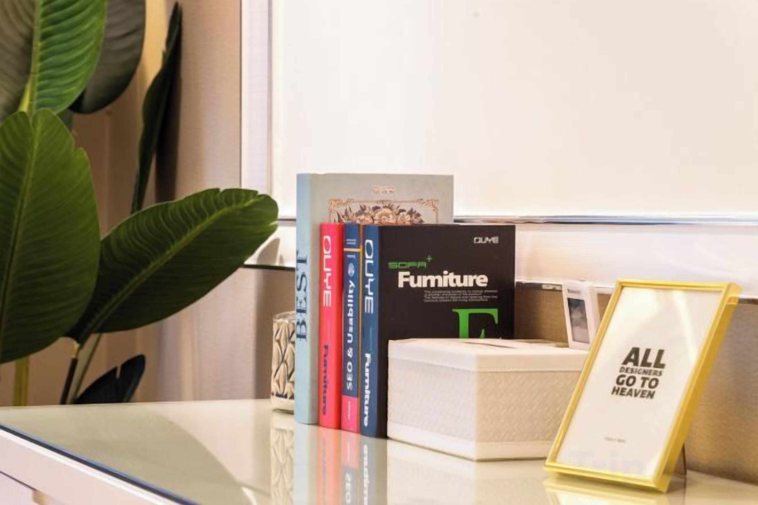 Uma escrivaninha com uma planta, uma placa emoldurada e uma pilha de livros.