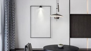 Een moderne eetruimte met een ronde tafel, een stoel, een hanglamp en een lijst met een afbeelding aan de muur.