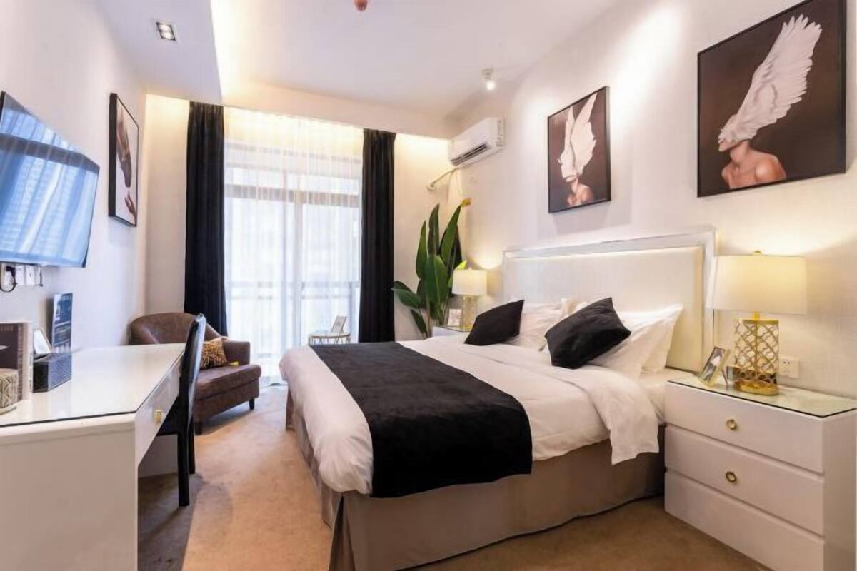 A hotel room with a bed, bedside tables, a desk, a chair, and a large window with curtains.