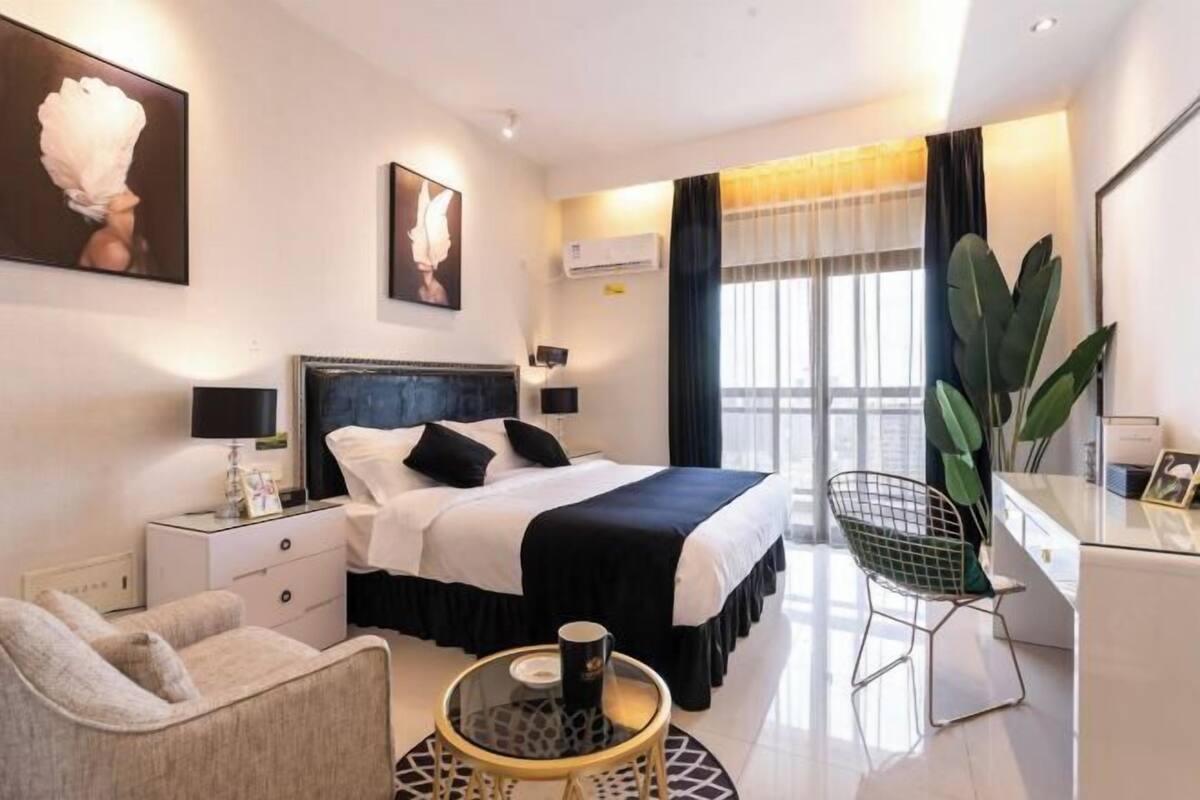 A modern hotel room with a large bed, a desk, a chair, and a round table.