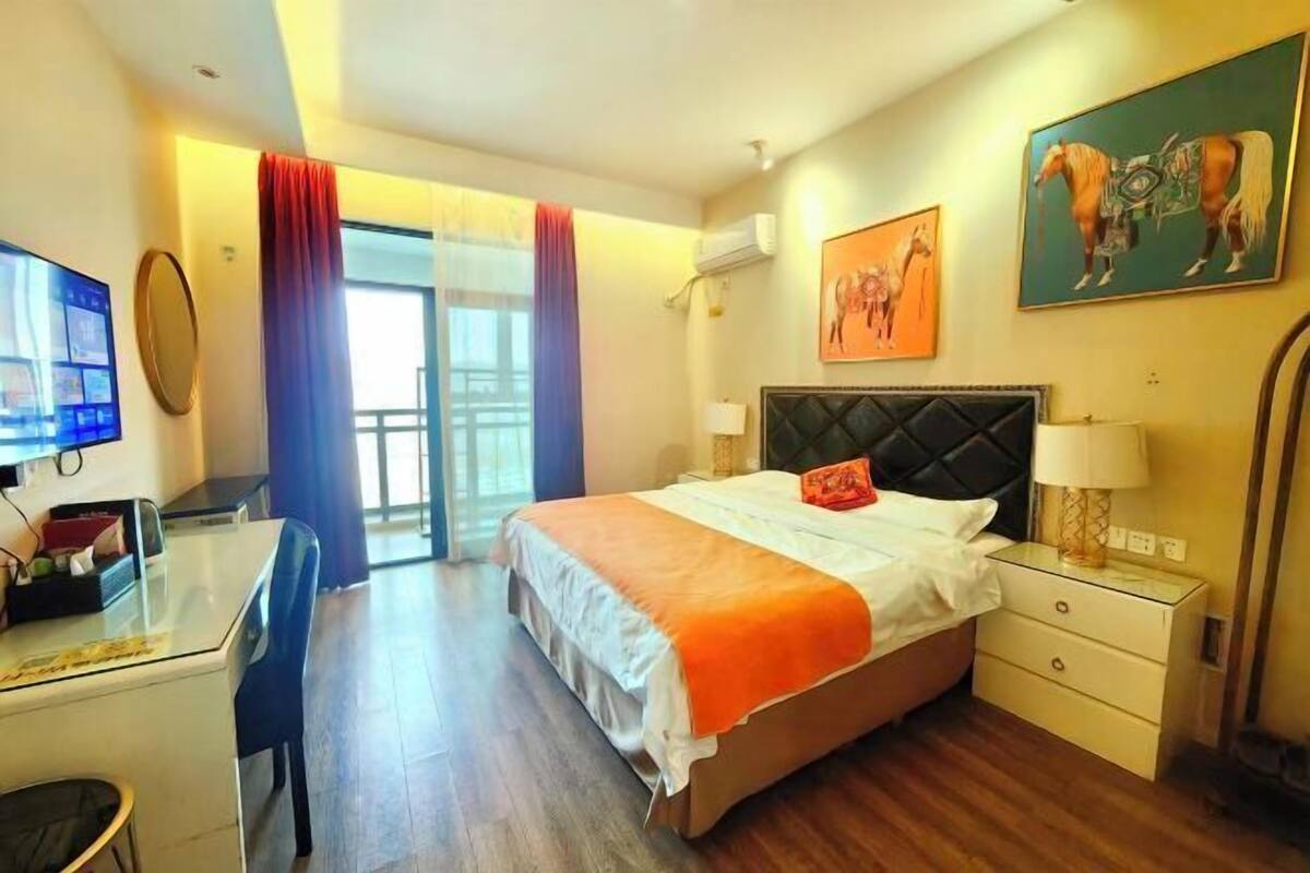 A hotel room with a bed, a desk, a chair, a TV, a window with curtains, and artwork on the walls.