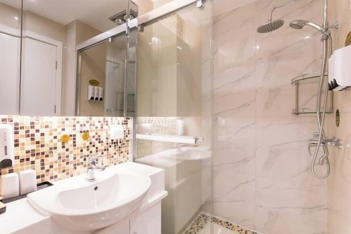 Une salle de bain moderne avec une douche à parois de verre, un lavabo blanc et un mur recouvert de mosaïques.