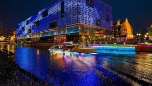 Een modern gebouw met een unieke gevel, een boot afgemeerd aan de waterkant, en een rivier op de voorgrond.