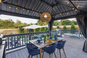 An outdoor deck with a table set for dining, surrounded by chairs, and a hanging light fixture above.