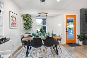 A dining area with a wooden table set for four, surrounded by black chairs, a potted plant, and a framed picture on the wall.