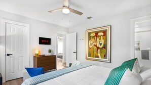 A modern bedroom with a bed, a ceiling fan, a painting, and a television displaying 'NETFLIX'.