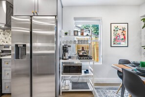 A modern kitchen with a stainless steel refrigerator, a built-in coffee maker, and a window with a view of greenery. - Family Getaway w/ Pizza Oven, Hot Tub, Mini Golf & BBQ Near Kalahari (Round Rock)