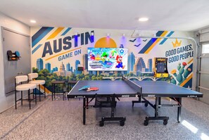 A gaming room with a large screen, two ping pong tables, and a mural with gaming characters. - Family Getaway w/ Pizza Oven, Hot Tub, Mini Golf & BBQ Near Kalahari (Round Rock)