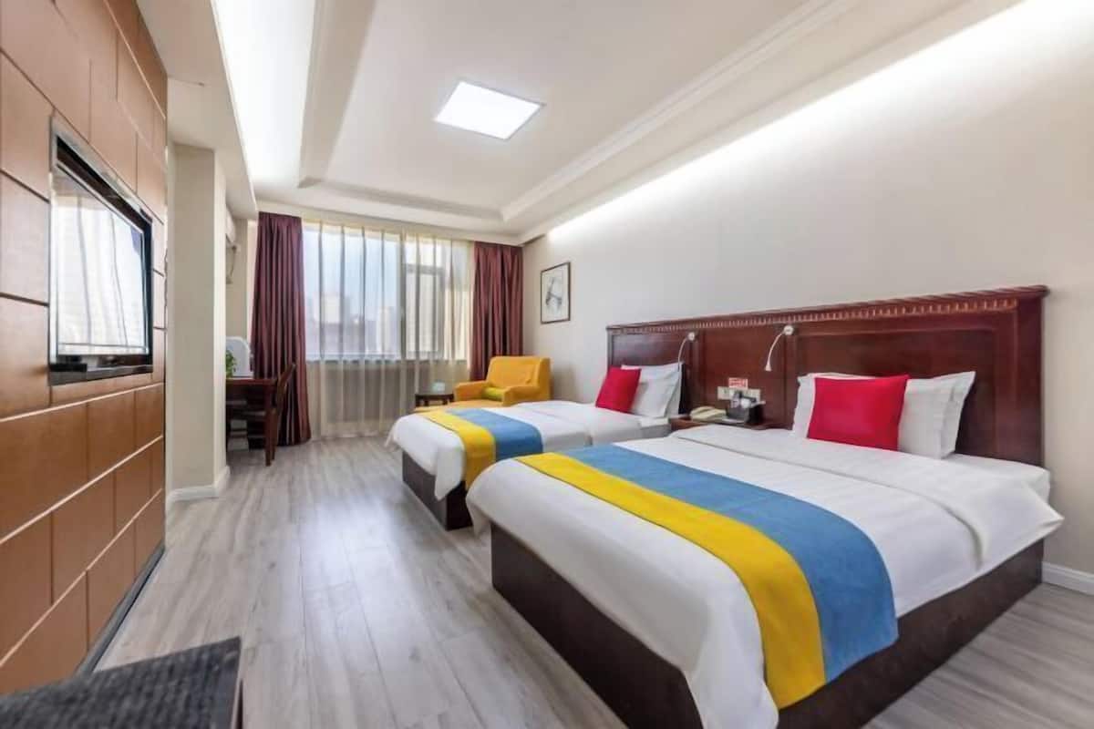 Habitación de hotel con dos camas, televisión, escritorio y ventana con cortinas.