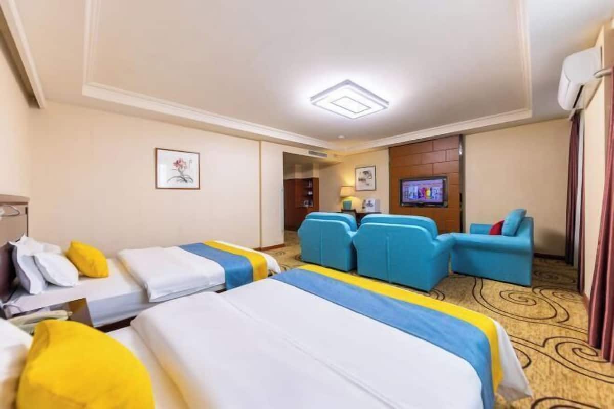 Habitación de hotel con dos camas, un sofá, un televisor y una kitchenette pequeña.
