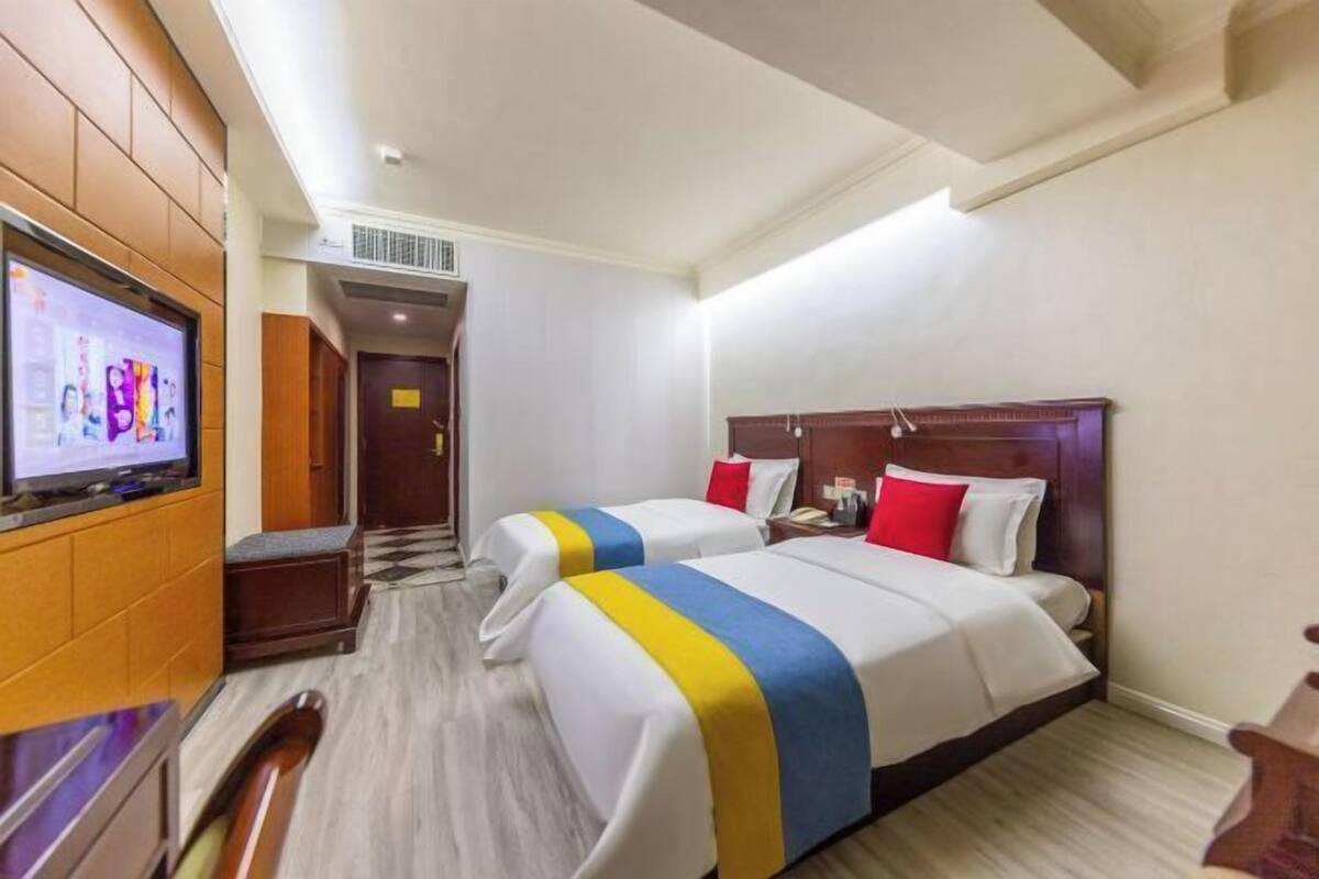 Habitación de hotel con dos camas, un televisor a la izquierda y un cabecero de madera.