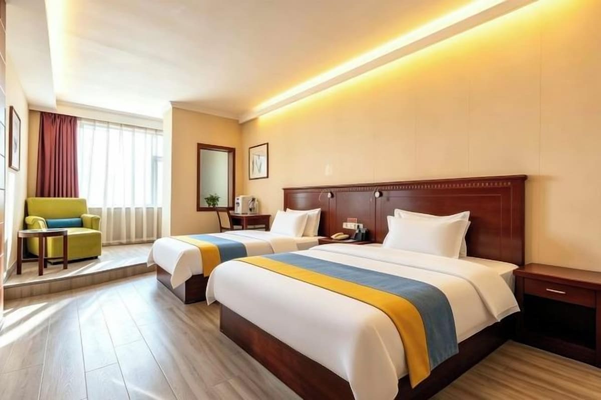 Une chambre d’hôtel avec deux lits, un bureau, une chaise et une fenêtre avec des rideaux.