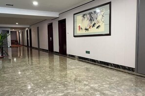 Un pasillo con piso de mármol pulido, obras de arte en la pared y puertas que dan a varias habitaciones.