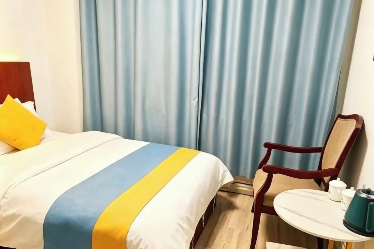 Une chambre d’hôtel avec un lit, une chaise, une petite table et un rideau.