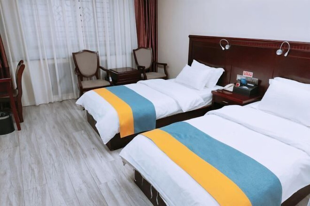 A hotel room with two beds, a wooden headboard, a small table with a telephone, and a chair.