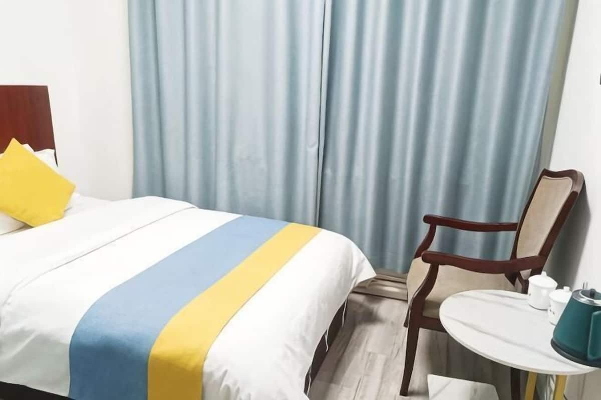 Una habitación de hotel con una cama, una silla, una mesita y una cortina.